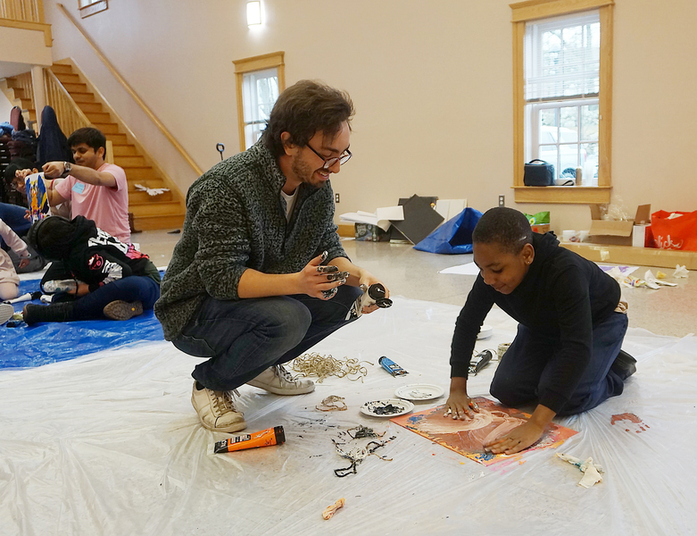 Charlie Shvartsman helps a child smearing colorful paint with his fingers on a piece of paper.