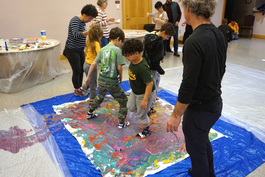 4 children wearing socks walk around on a large piece of white paper covered in paint.