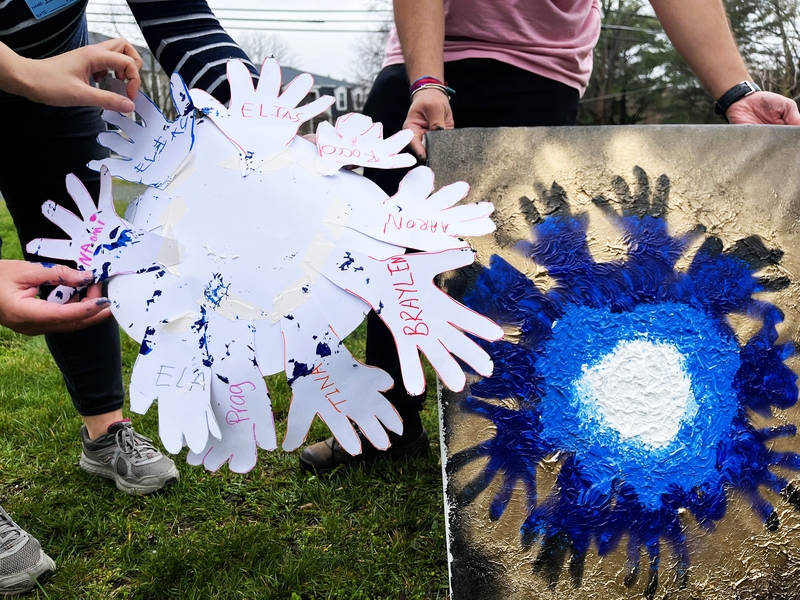 A circular arrangements of paper cutouts of children's hands is held next to a spray-painted painting in the same shape.